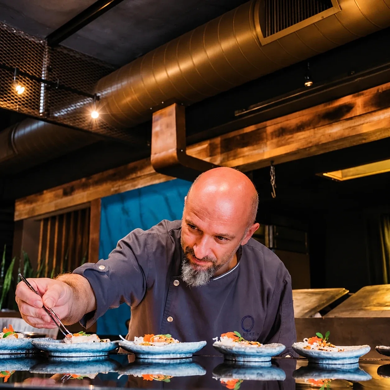 Chef Nicola Allegretta plating a row of small dishes with tweezers at Mistura